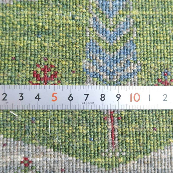 緑と青の繊細な模様が特徴の手織りウールラグが、定規と共に撮影され、ギャッベの密な織り目が際立っている。