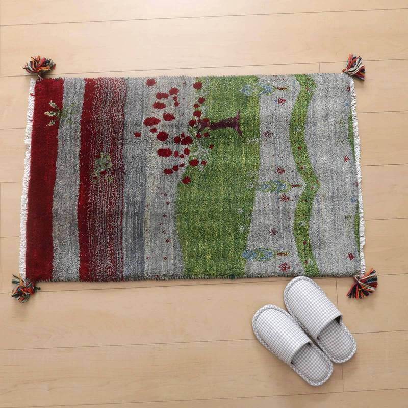 色とりどりの模様が魅力的な手織りのギャッベラグが、ナチュラルな木目の床に調和し、隣には白いスリッパが置かれている。
