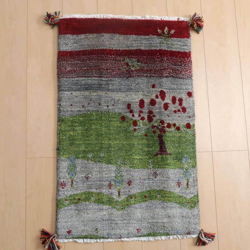 ギャッベ／ルリバフ 90×57cm（HSS-72576）は、鮮やかな赤と緑の模様が美しい手織りウールのギャッベラグが、木目の床にしっかりと敷かれている。