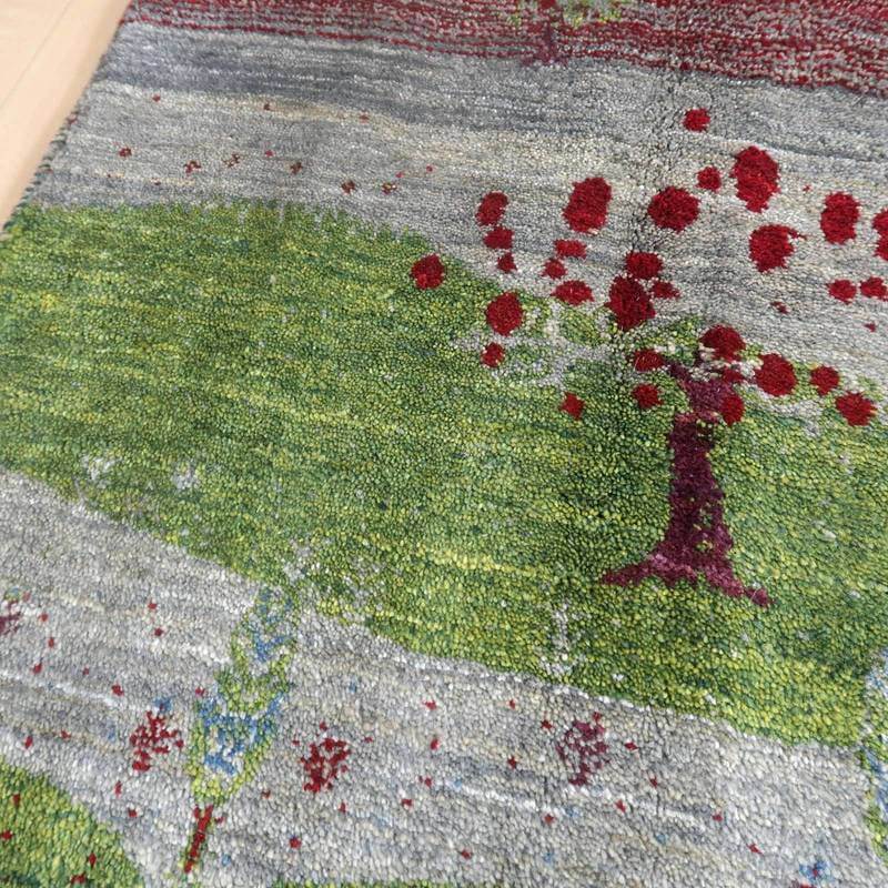 緑豊かな風景と赤い花が丁寧に手織りされたギャッベのラグが、ウールの温かみを感じさせるように床に敷かれている。
