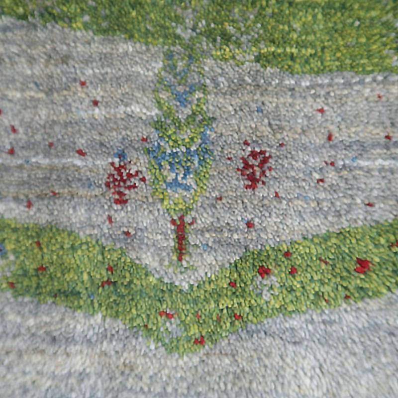 緑とグレーの色調が美しい手織りのギャッベラグには、赤い花模様が丁寧に織り込まれ、ウールの温かみが感じられる。