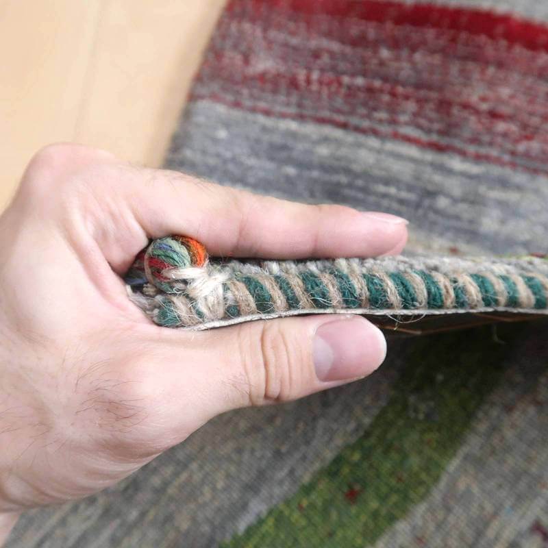 手に持たれたギャッベの厚みと織りの密度が分かる接写で、鮮やかな色彩とウールの質感が際立っている。