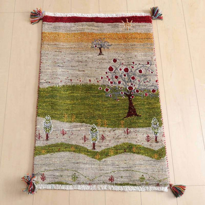 ギャッベ／ルリバフ 86×59cm（HSS-73062）は、色鮮やかな木々と自然の風景が描かれた手織りのギャッベラグが、ウールの豊かな質感を通して床に置かれている。