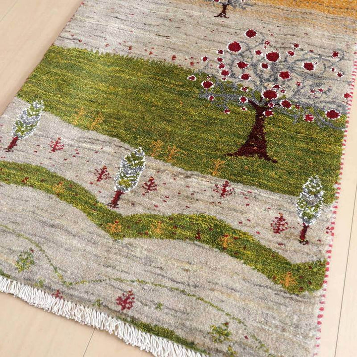 緑豊かな風景が描かれた手織りのギャッベラグが、ウールの温かみとともに床に広がっている。