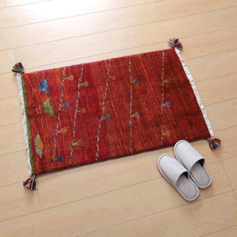 赤い手織りのギャッベラグが床に敷かれ、カラフルな模様が温かみを添えるペルシャ絨毯専門店の通販商品が見える。