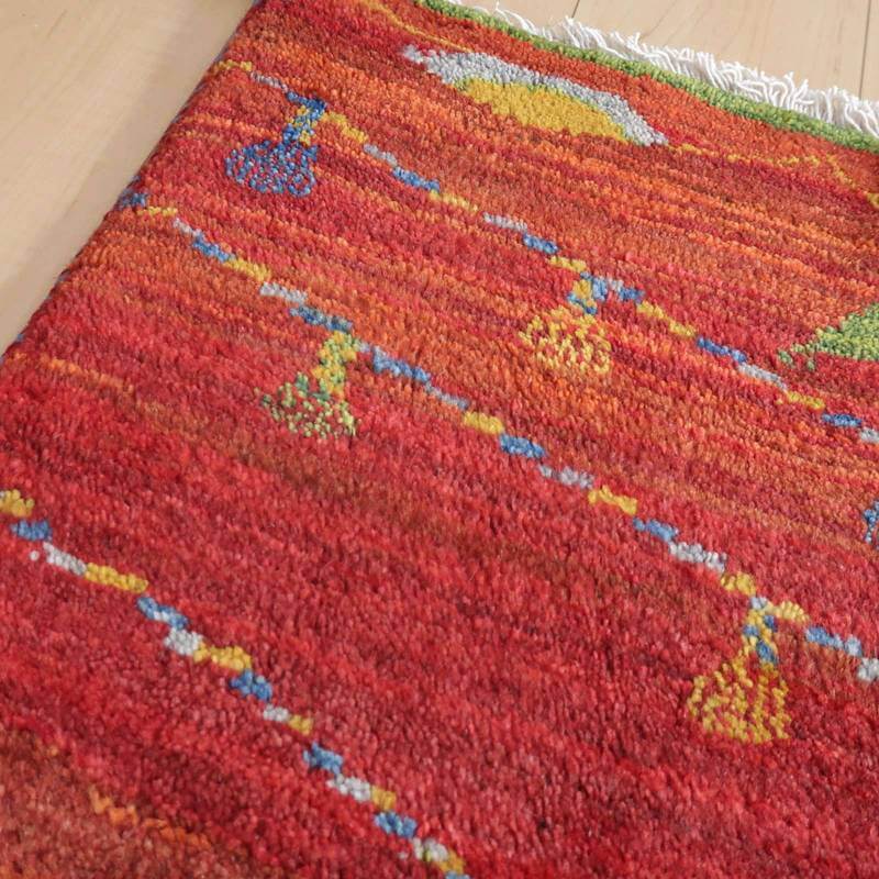 赤を基調にカラフルな模様が丁寧に手織りされたギャッベのラグが、ウールの柔らかさを感じさせながら床に広がっている。