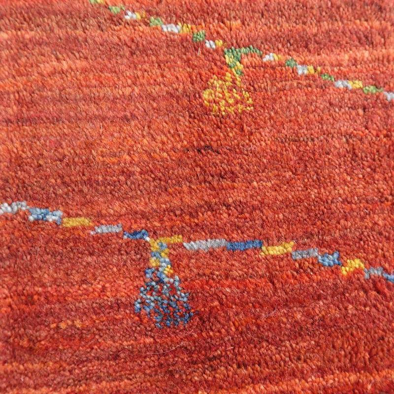 暖かみのある赤いウール素材のギャッベラグが、手織りのペルシャ絨毯特有の繊細な模様とともに床に広がっています。