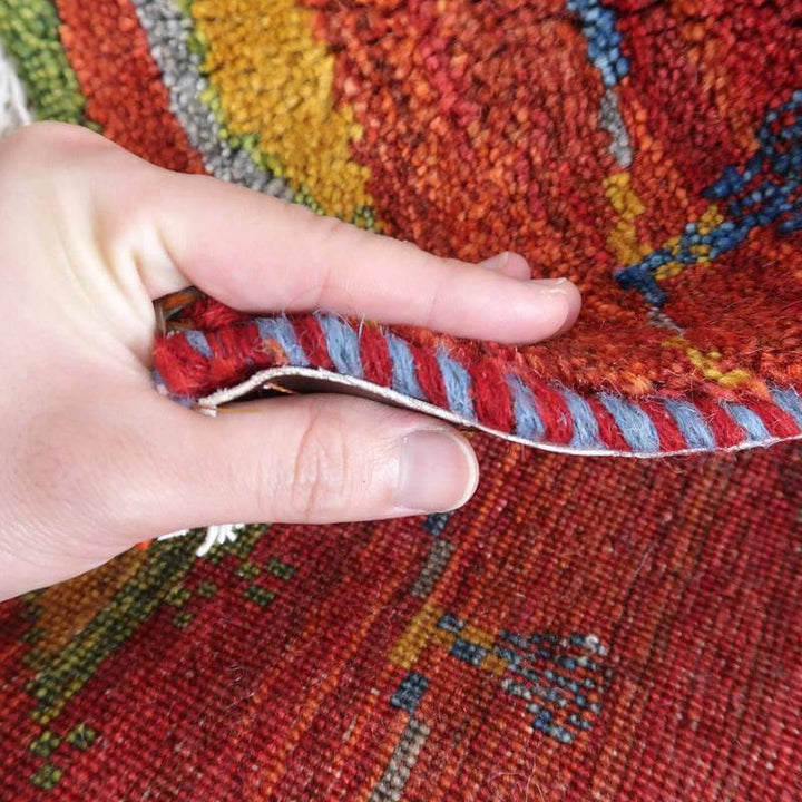 手織りのギャッベラグが丁寧にめくられ、ウールの柔らかさとカラフルな模様が際立っている。