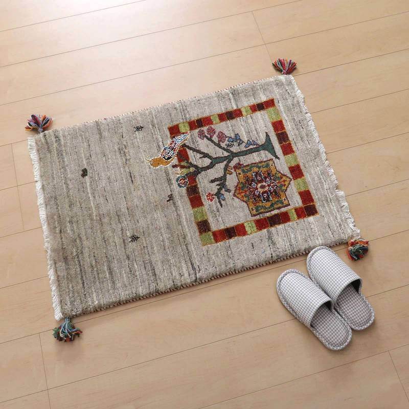 手織りのギャッベラグが明るい木目の床に敷かれ、色鮮やかな柄が温かみを添え、隣にはシンプルなスリッパが置かれている。