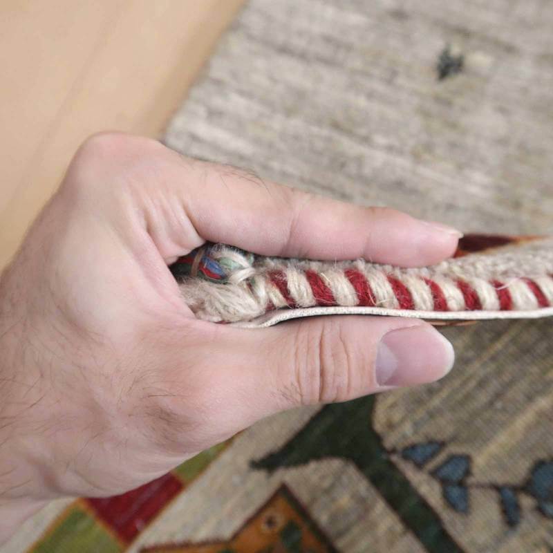 手に持たれたギャッベのラグが、丁寧に手織りされたウールの密度と厚みを感じさせ、ペルシャ絨毯の専門店ならではの質感が際立っている。