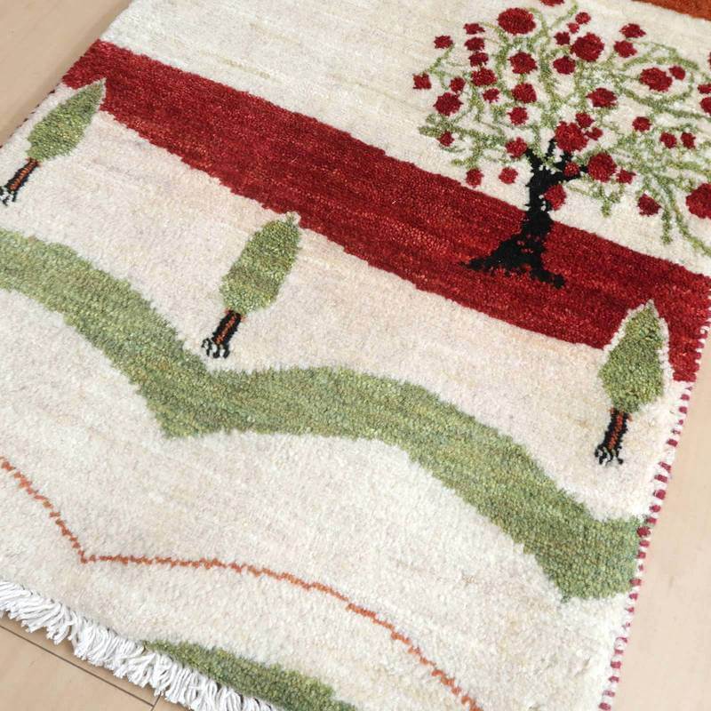 手織りのギャッベラグが、緑と赤の自然モチーフで彩られたペルシャ絨毯専門店の通販商品として床に映えている。