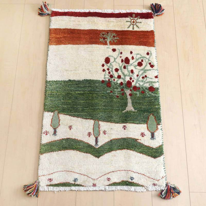 ギャッベ／ルリバフ 84×52cm（HSS-73193）は、赤と緑の自然モチーフが美しくデザインされた手織りのギャッベラグが、木の床にしっくりと敷かれている。