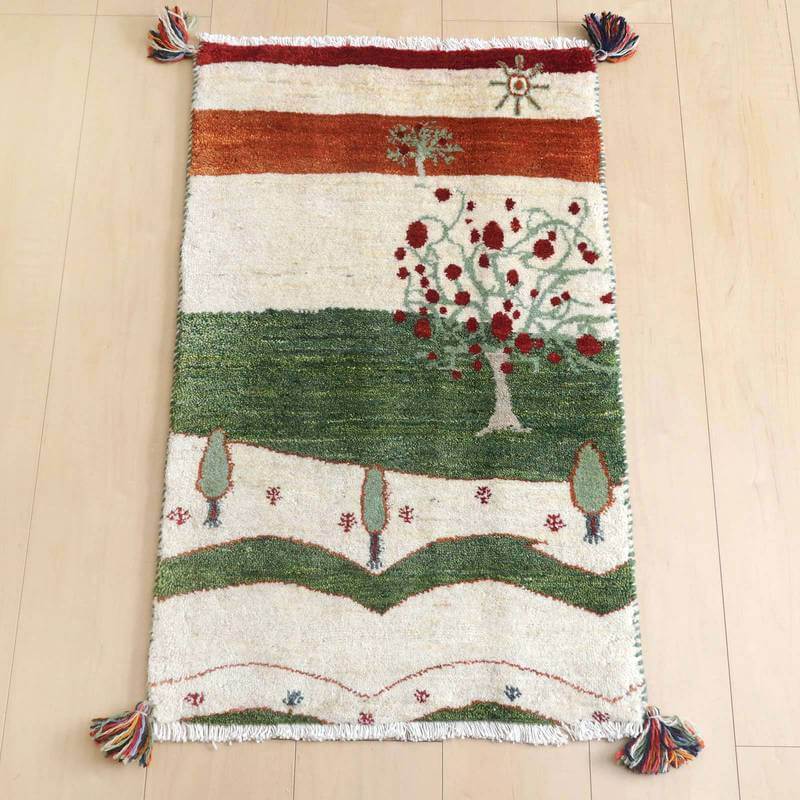 ギャッベ／ルリバフ 84×52cm（HSS-73193）は、赤と緑の自然モチーフが美しくデザインされた手織りのギャッベラグが、木の床にしっくりと敷かれている。