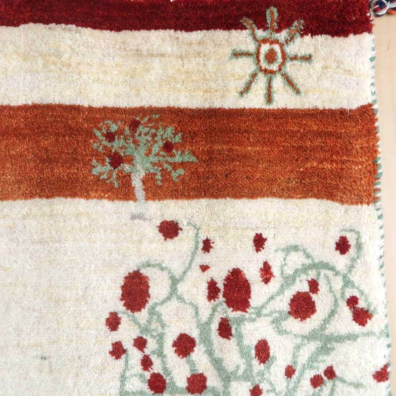 手織りのウール製ギャッベラグには、赤と白のコントラストが美しいペルシャ絨毯特有の模様が描かれており、専門店で通販可能な一枚が際立っている。