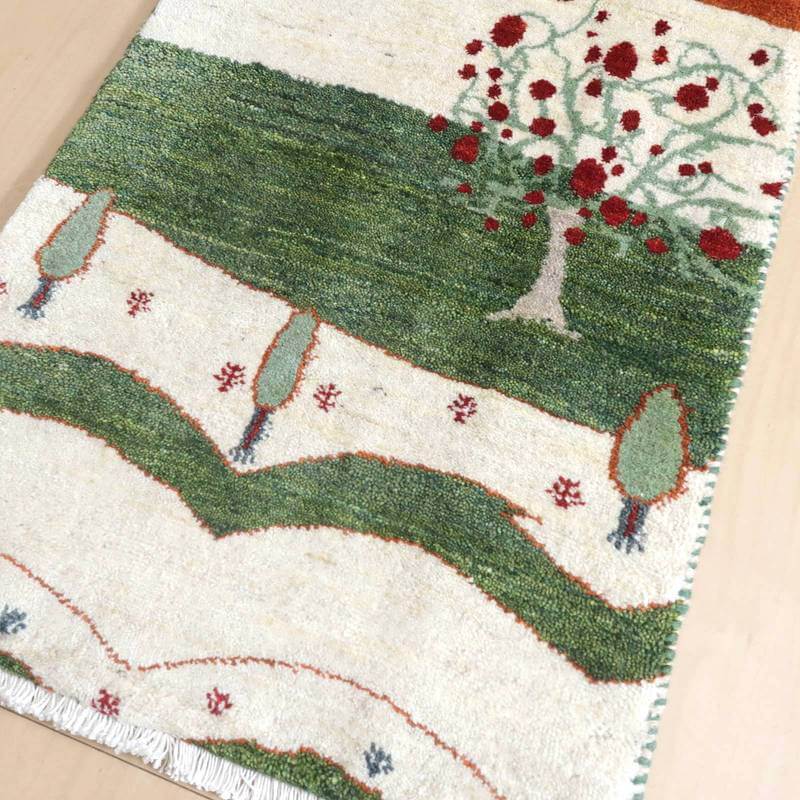 手織りのギャッベラグが緑と赤の模様で彩られたペルシャ絨毯専門店の一品で、ウール素材が温かみを感じさせるデザインが床に広がっている。