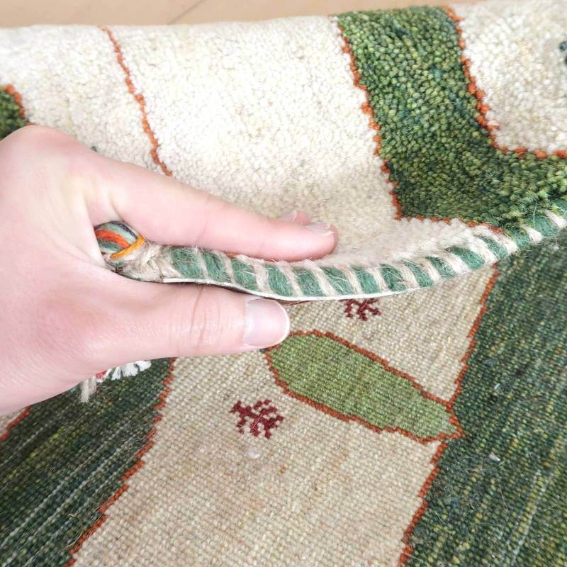 丁寧に手織りされたペルシャ絨毯のギャッベが、ウールの温かみと緻密な織り目を見せつつ、通販専門店での購入を考えさせる一枚がめくられている。