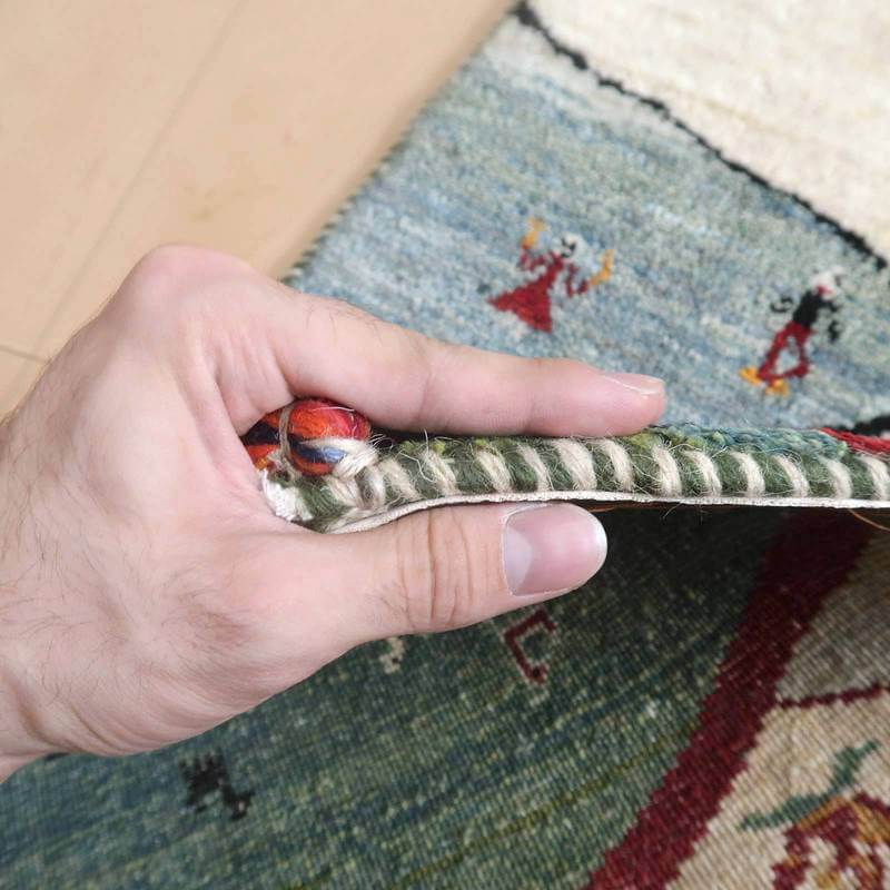 手織りのギャッベラグが持ち上げられ、細やかなウールの織り目とペルシャ絨毯の伝統的な模様が間近に見える。