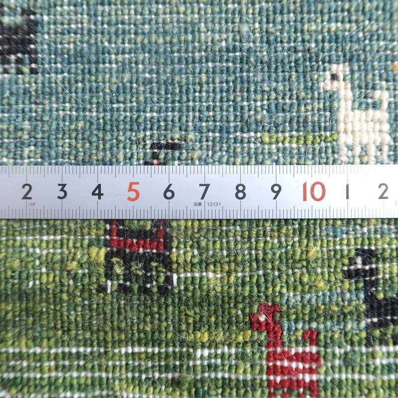 緑を基調に赤や白の模様が織り込まれた手織りウールのギャッベラグが、定規と並んで繊細な織り目の密度が際立っている。