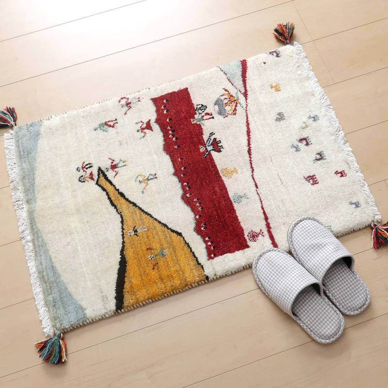 温かみのあるデザインが魅力的な手織りのウールギャッベラグが、玄関でスリッパとともに床に置かれている。