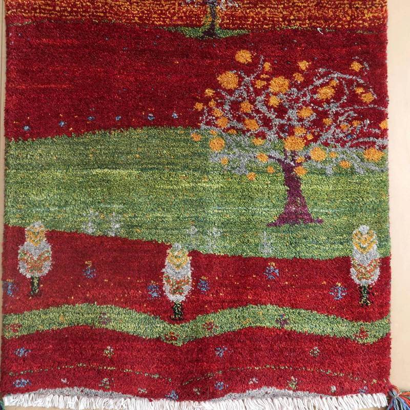鮮やかな赤と緑のコントラストが美しい手織りのギャッベラグは、ウール素材の柔らかな質感とペルシャ絨毯ならではの繊細な樹木模様が際立っている。