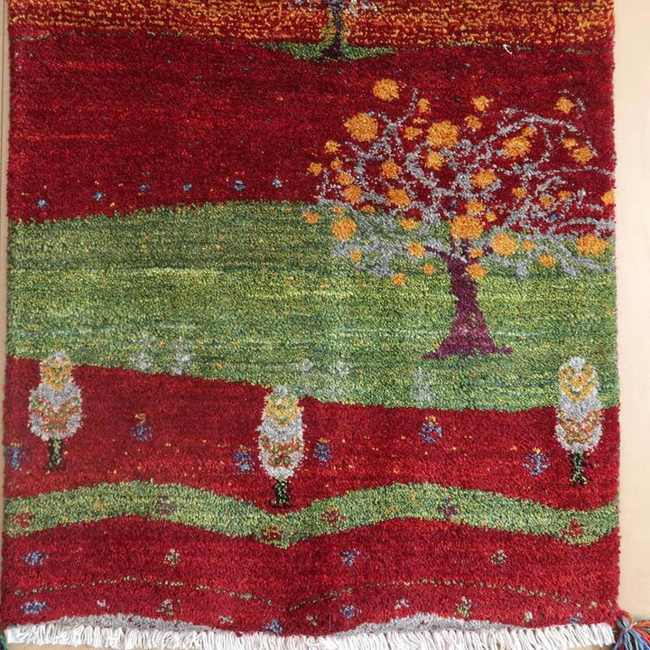 鮮やかな赤と緑のコントラストが美しい手織りのギャッベラグは、ウール素材の柔らかな質感とペルシャ絨毯ならではの繊細な樹木模様が際立っている。