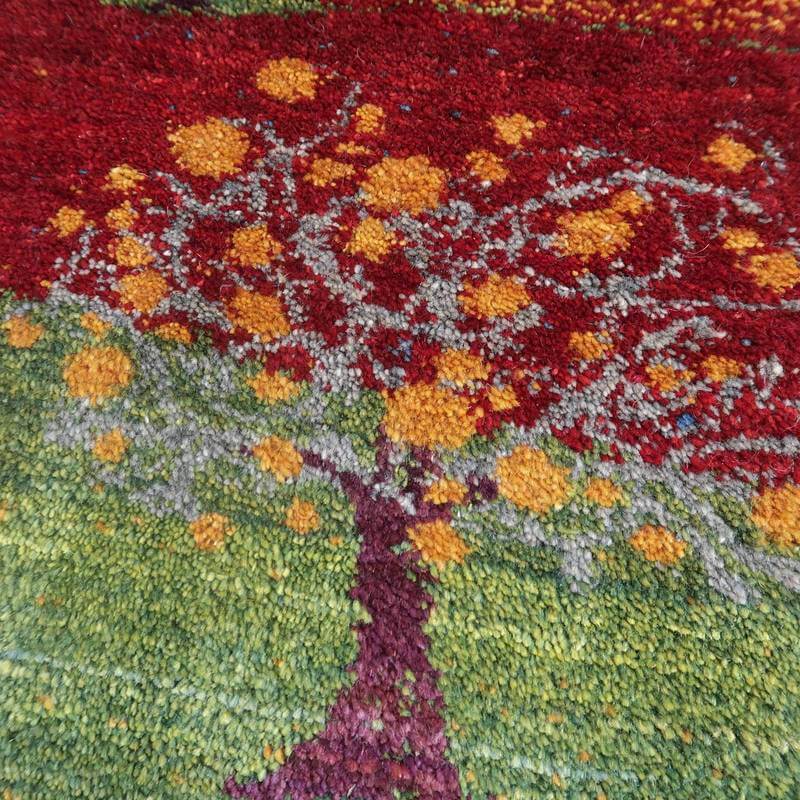 色鮮やかな赤と緑のウールで丁寧に手織りされたギャッベのラグ、木の模様が華やかに描かれている。