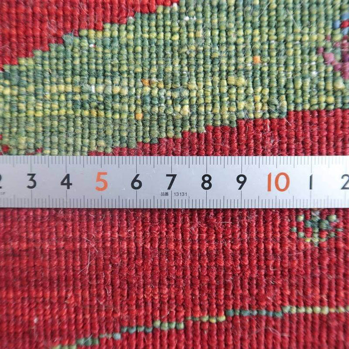 赤と緑の色合いが美しい手織りウールのギャッベラグは、ペルシャ絨毯専門店の通販で購入可能で、織りの密度が定規で詳細に測定されている。
