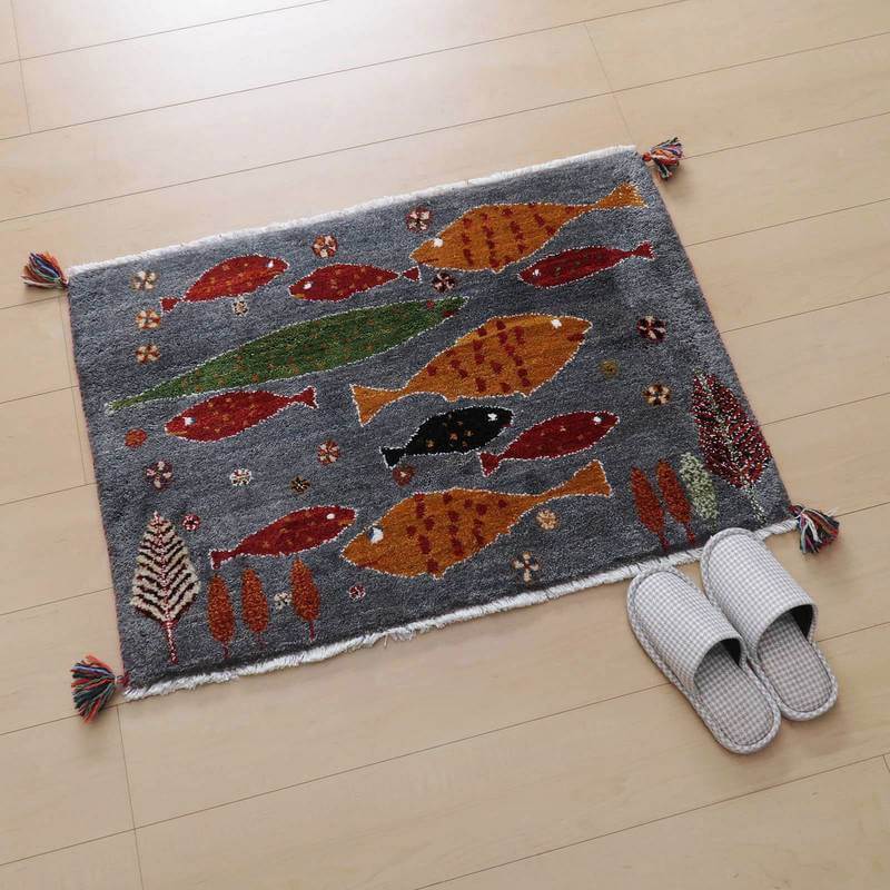 ギャッベ／ルリバフ 63×90cm（HSS-77703）は、手織りのウール素材で描かれた色とりどりの魚たちが、玄関の床に優雅に並ぶギャッベラグが見える。