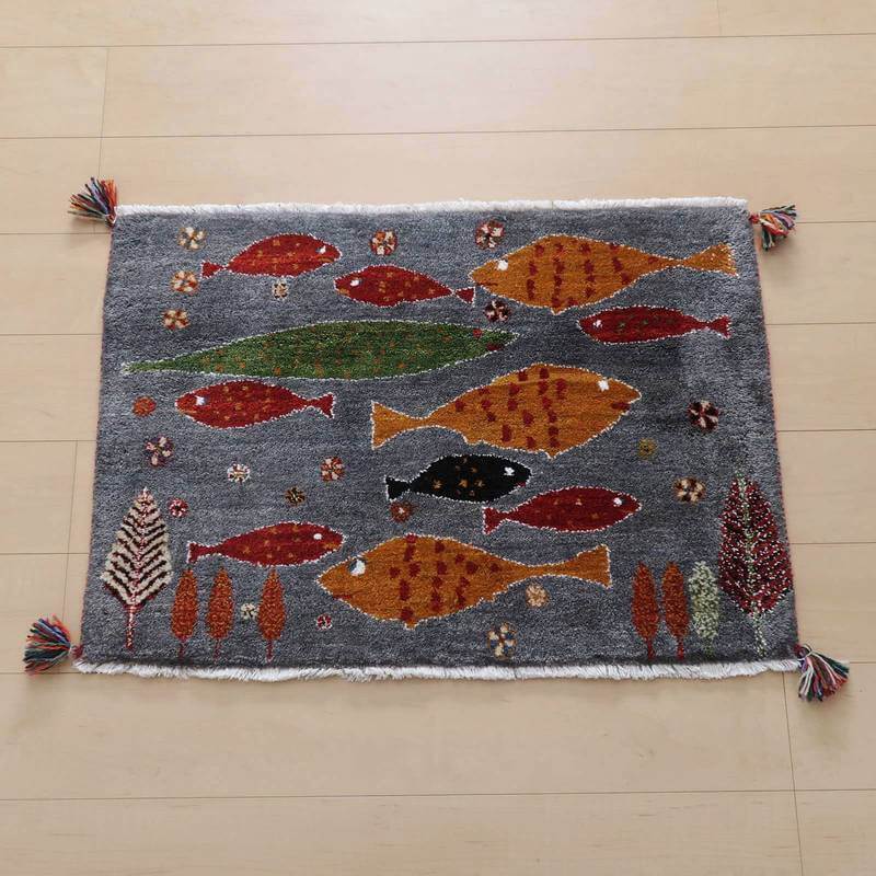 色とりどりの魚と自然モチーフが描かれた手織りのウール製ギャッベラグが、床に美しく広がり、ペルシャ絨毯の専門店で通販されている様子が見える。