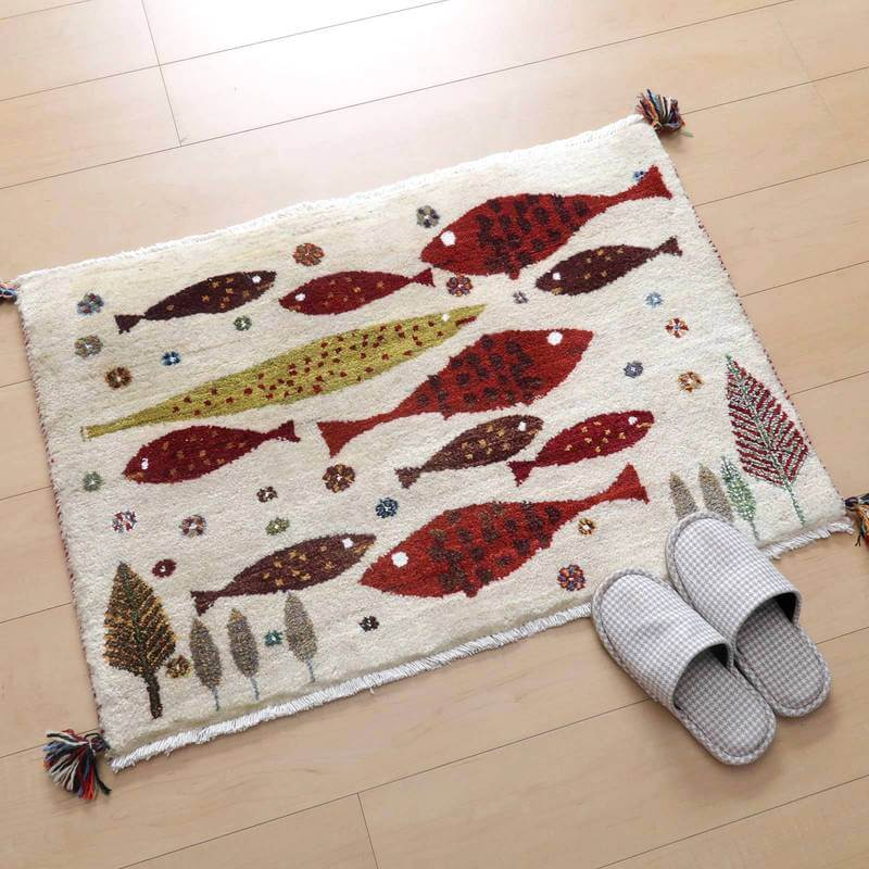 カラフルな魚と木々が丁寧に手織りされたウール素材のギャッベラグが、木目調の床に鮮やかに敷かれている。