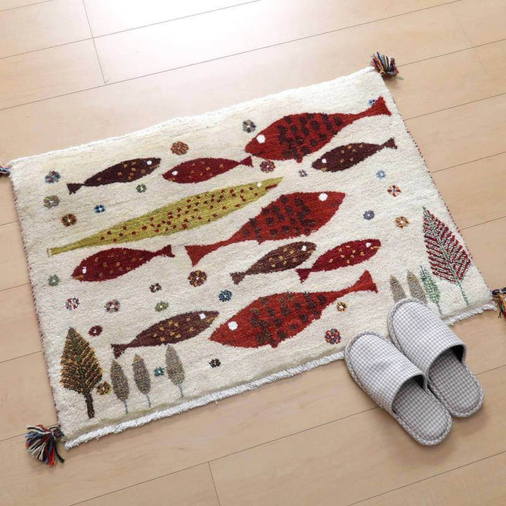 カラフルな魚と木々が丁寧に手織りされたウール素材のギャッベラグが、木目調の床に鮮やかに敷かれている。