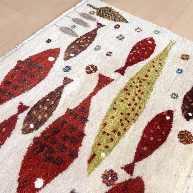 赤や緑の魚が描かれた手織りのギャッベラグが床に敷かれ、ウールの温かみとペルシャ絨毯の魅力が際立っている。