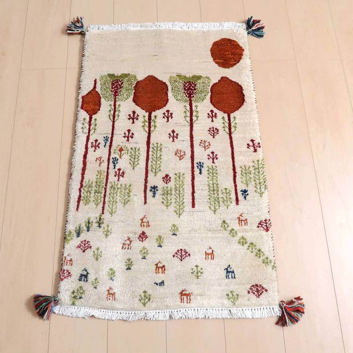 ギャッベ／ルリバフ 90×58cm（HSS-77756）は、手織りの温かみを感じるギャッベラグが木の模様と動物のデザインで彩られ、ウール素材の柔らかさが床に映える様子が見える。