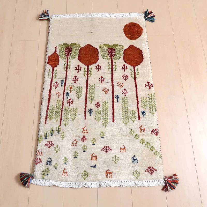 ギャッベ／ルリバフ 90×58cm（HSS-77756）は、手織りの温かみを感じるギャッベラグが木の模様と動物のデザインで彩られ、ウール素材の柔らかさが床に映える様子が見える。