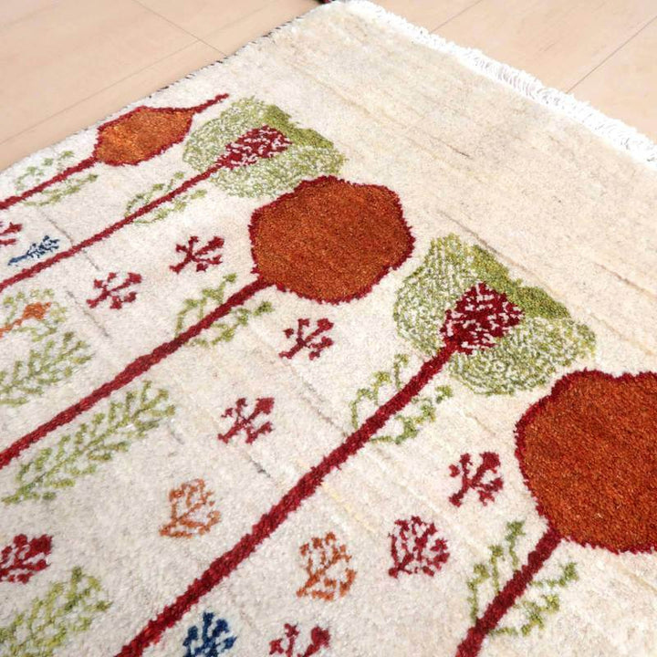 生成したaltテキスト: 色鮮やかな花模様が丁寧に手織りされたウール製のギャッベラグが床に柔らかく敷かれている。