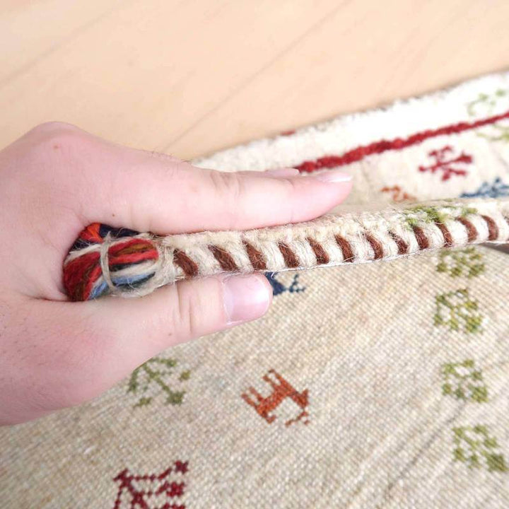 手織りのギャッベラグの厚みと織り目の密度が丁寧に示され、ウールの柔らかい質感が手に伝わる様子が見える。