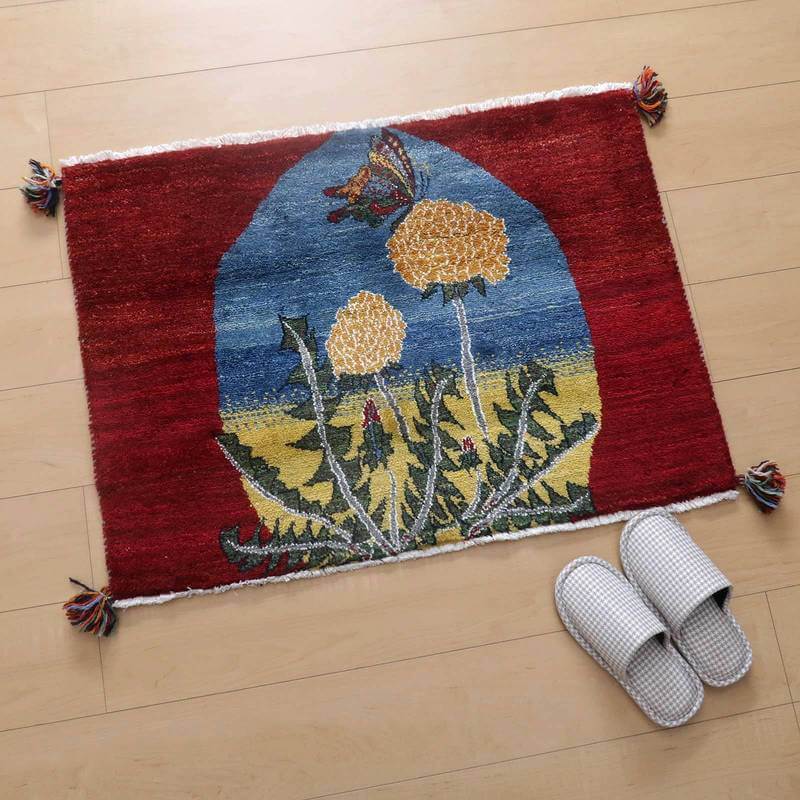 ギャッベ／ルリバフ 64×88cm（HSS-777691）は、赤と青の背景に黄色の花が描かれた手織りのギャッベラグが、木目調の床にぬくもりを添えて敷かれている。