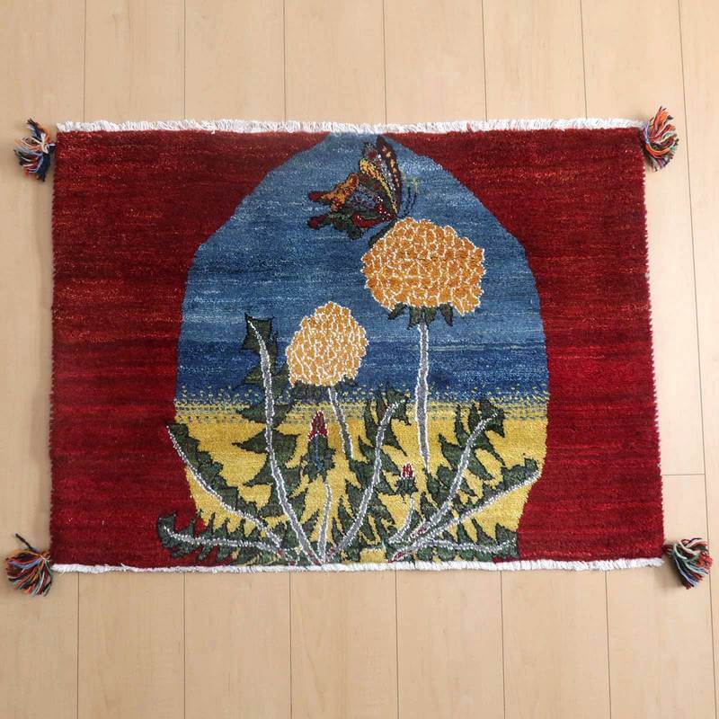 鮮やかな赤地に黄色い花が描かれた手織りのギャッベラグが、木目の床にしっかりと敷かれている。