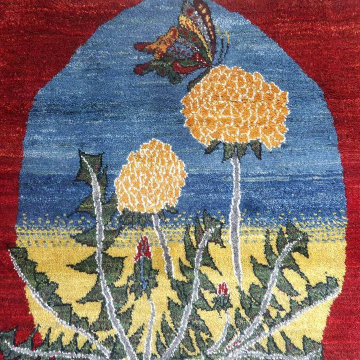 赤と青の背景に黄色い花と蝶が描かれた手織りのギャッベラグが、繊細なウールの織り目と共に際立っている。