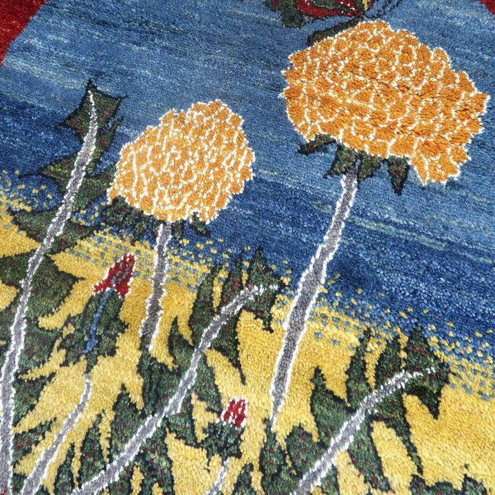 青と黄色の背景に鮮やかな花模様が描かれた手織りのギャッベが、ウールの繊細な質感とともに際立っている。