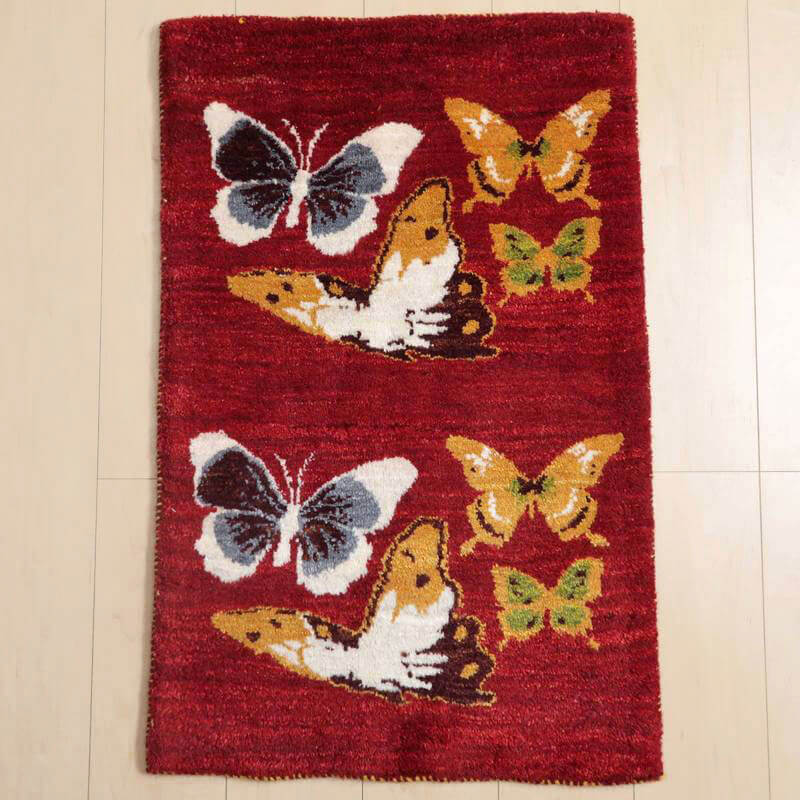 ギャッベ／ルリバフ 87×57cm（HSS-89459）は、赤いウールの手織りラグに、色とりどりの蝶々が舞う華やかな模様が施され、ペルシャ絨毯専門店の通販で提供されるギャッベが床に広がっている。