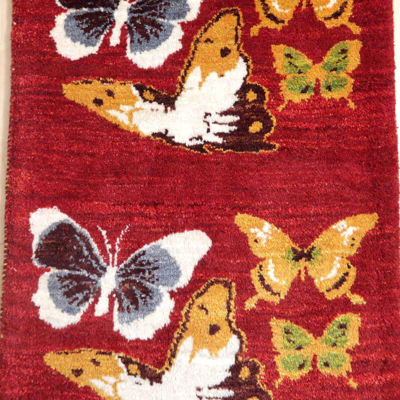 赤地にカラフルな蝶が舞うデザインのギャッベラグは、手織りの温かみとペルシャ絨毯の伝統が感じられる専門店通販アイテムが魅力的に敷かれている。