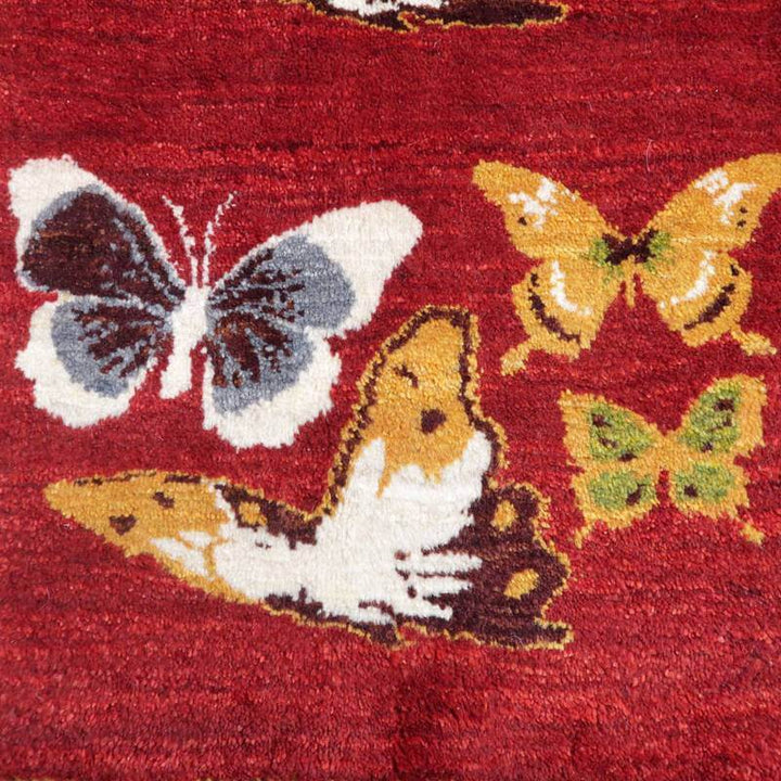 赤い手織りのウール製ギャッベに描かれた色とりどりの蝶が、ペルシャ絨毯専門店の通販で見られる。
