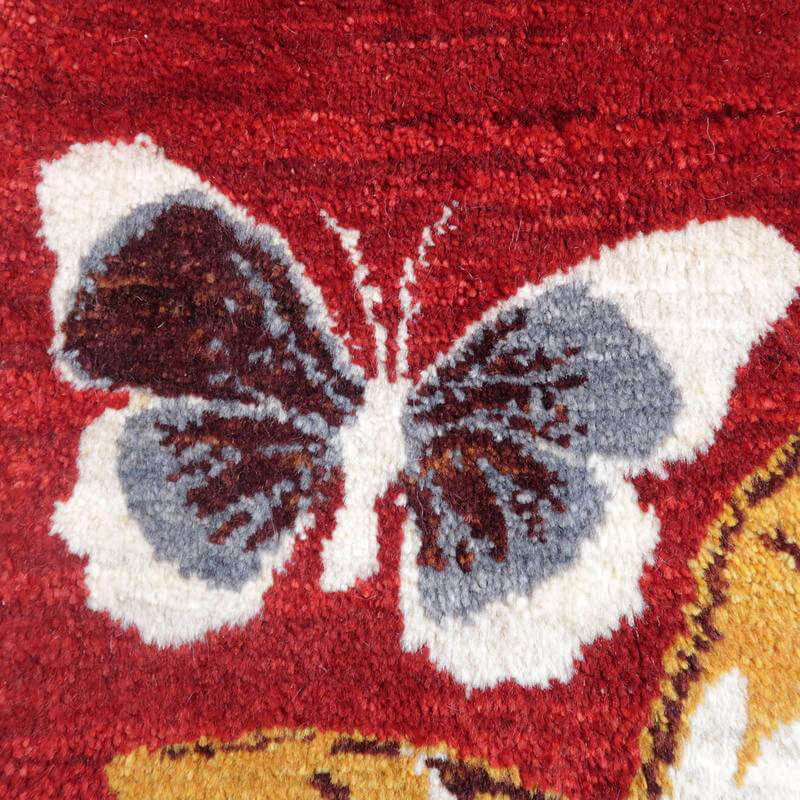 赤い背景に美しく描かれた蝶の模様が印象的な手織りのギャッベラグが、ペルシャ絨毯専門店の通販で温かみを添えている。