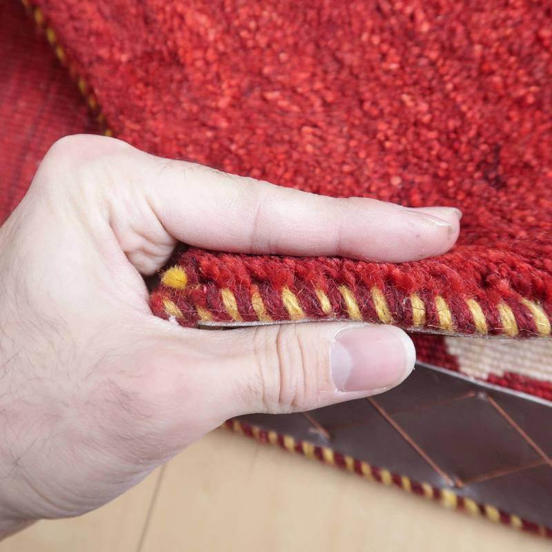 手に持たれた厚みのある赤い手織りギャッベラグの織り目が、ウールの温かみを感じさせます。