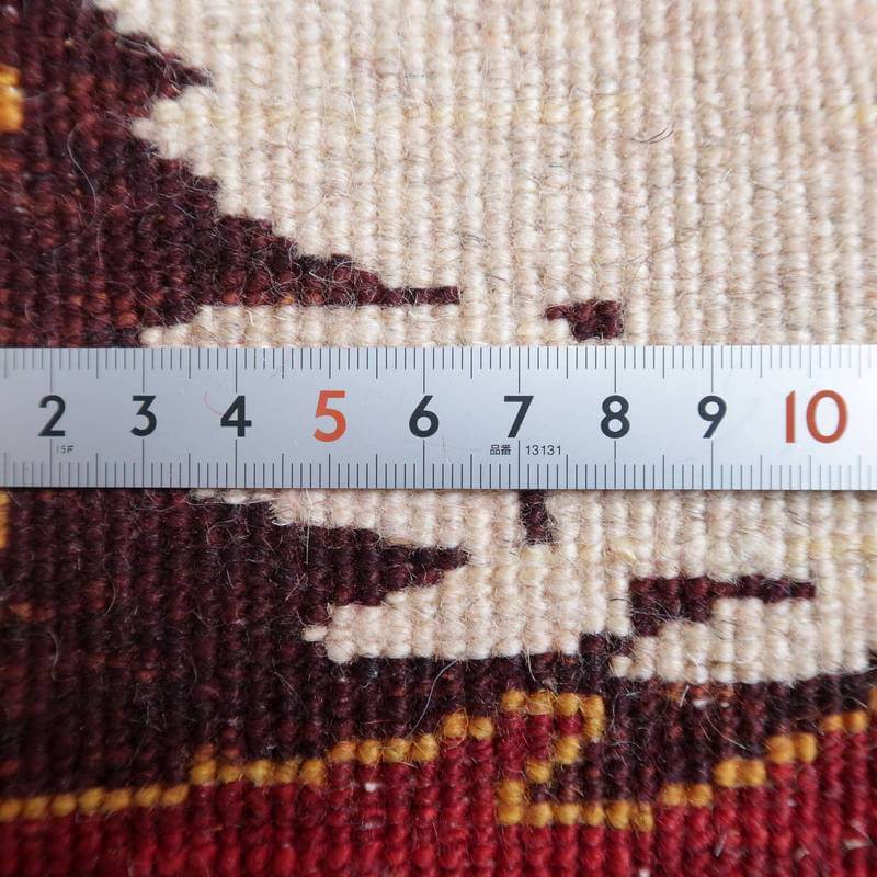 手織りのギャッベラグの織り目が定規で測定され、精巧なウールの質感とペルシャ絨毯専門店ならではの豊かな色彩が際立っている。