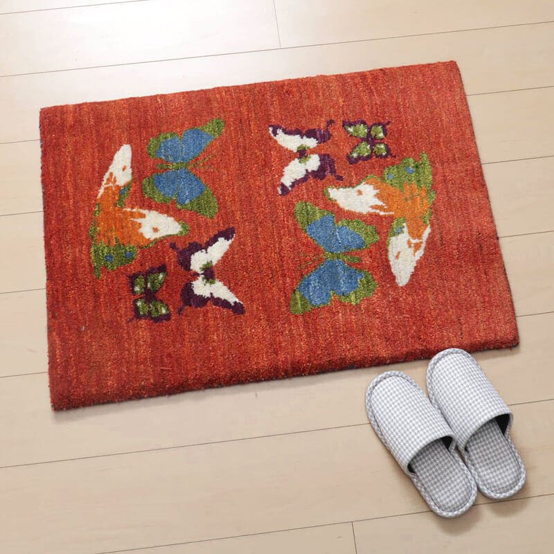 赤いギャッベラグの上に色とりどりの蝶が舞うデザインが施され、手織りの温もりが感じられるウール素材が床に優雅に敷かれている。