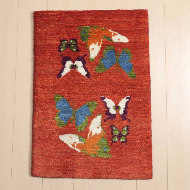 ギャッベ／ルリバフ 83×58cm（HSS-91223）は、色鮮やかな蝶のデザインが施された手織りのギャッベラグが、ウール素材で丁寧に仕上げられたペルシャ絨毯専門店の通販商品として床に美しく敷かれている。