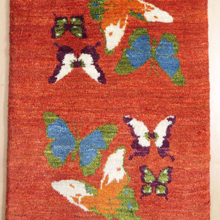 赤い背景に色とりどりの蝶が丁寧に描かれたウール製の手織りギャッベが、ペルシャ絨毯専門店の通販で見つかる。