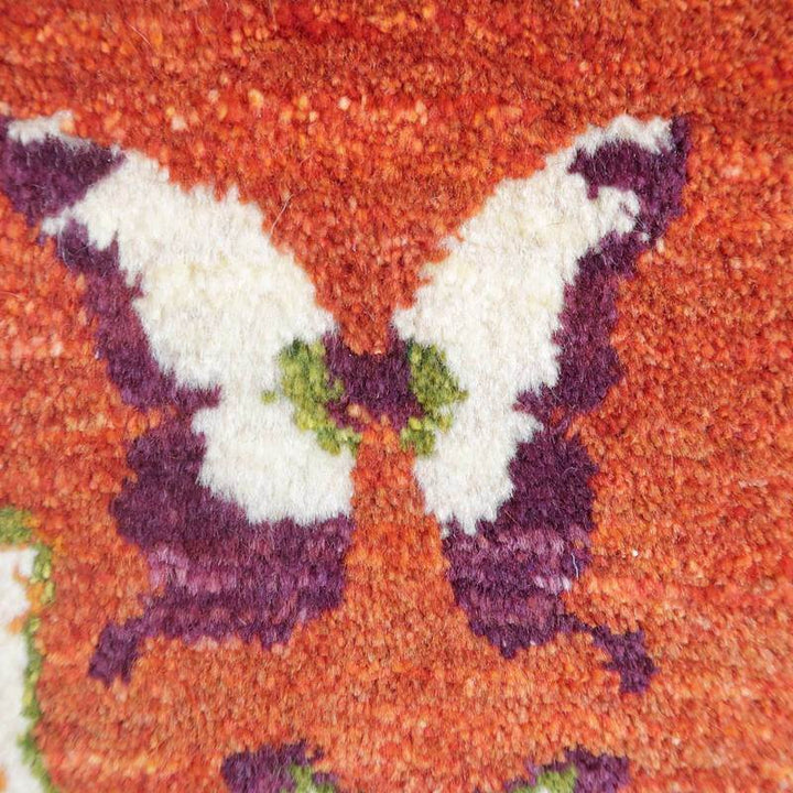 手織りのギャッベラグに描かれた蝶の模様が、オレンジと白のコントラストで生き生きと浮かび上がっている。